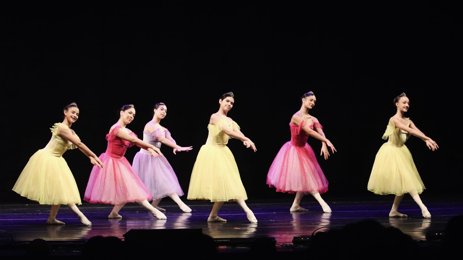 Seis bailarinas de saias românticas amarelas, rosas e lilás dançando em linha no palco do Theatro Carlos Gomes — MoviRio 2026